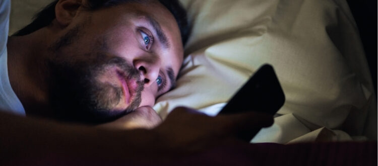 man looking at phone in bed