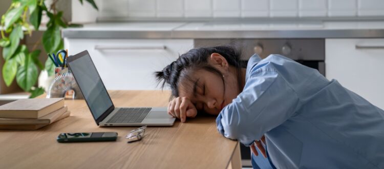 Woman with her head on her desk in front of her laptop